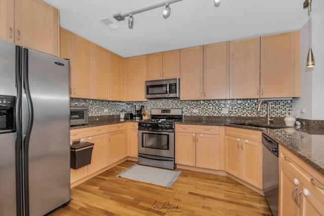 kitchen featuring light wood-type flooring, tasteful backsplash, stainless steel appliances, light brown cabinets, and dark stone countertops