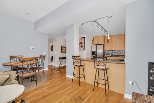 kitchen featuring stainless steel fridge with ice dispenser, backsplash, a breakfast bar area, stacked washer and clothes dryer, and light wood-type flooring