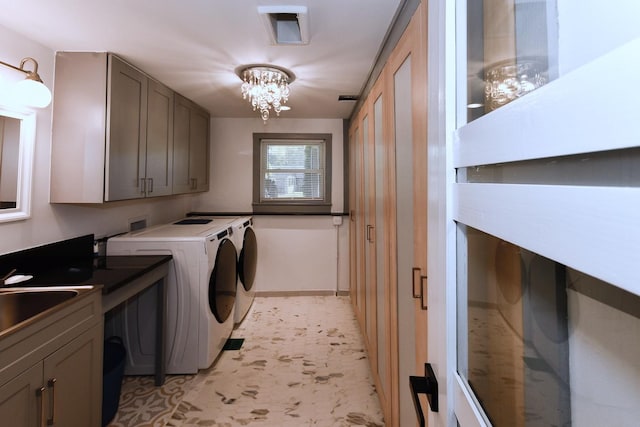 clothes washing area with a chandelier, washer and clothes dryer, cabinets, and sink