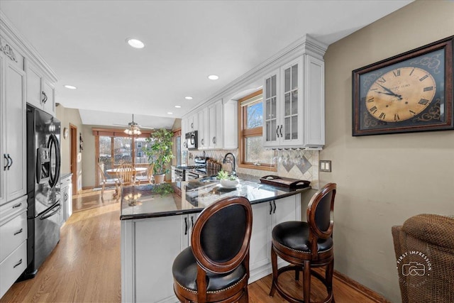 kitchen featuring black refrigerator with ice dispenser, kitchen peninsula, and white cabinetry