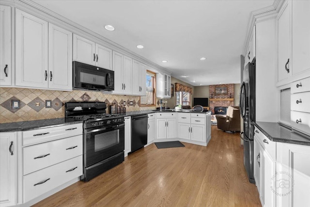 kitchen with light hardwood / wood-style floors, white cabinets, black appliances, and kitchen peninsula