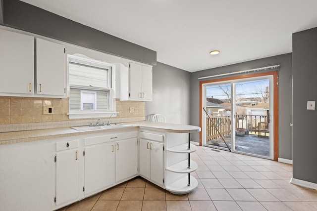 kitchen with sink, kitchen peninsula, light tile patterned floors, tasteful backsplash, and white cabinetry