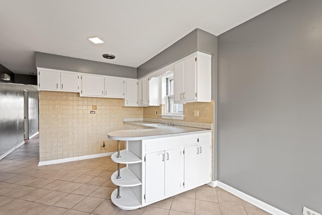 kitchen with kitchen peninsula, sink, white cabinets, and light tile patterned flooring