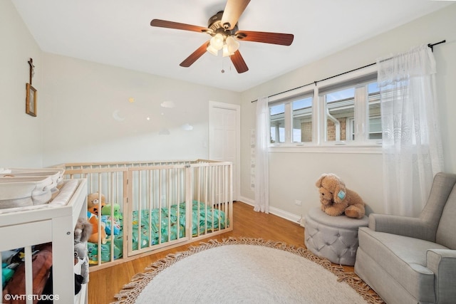 bedroom featuring ceiling fan, light hardwood / wood-style floors, and a crib