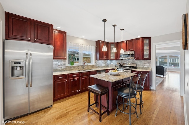 kitchen featuring appliances with stainless steel finishes, hanging light fixtures, a kitchen island, light hardwood / wood-style floors, and a kitchen bar