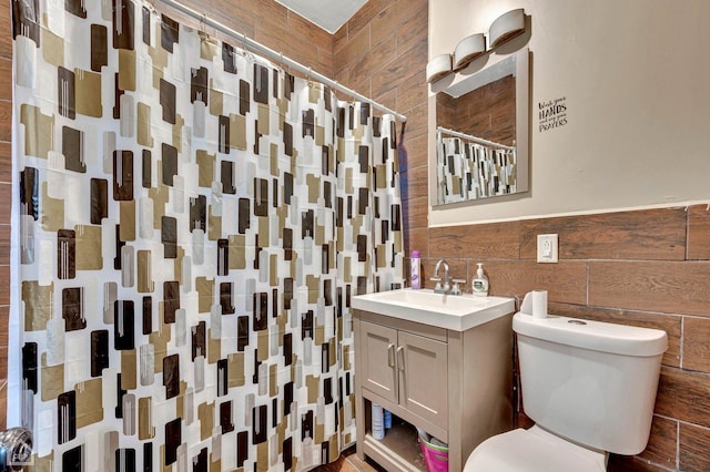 bathroom with curtained shower, wooden walls, vanity, and toilet