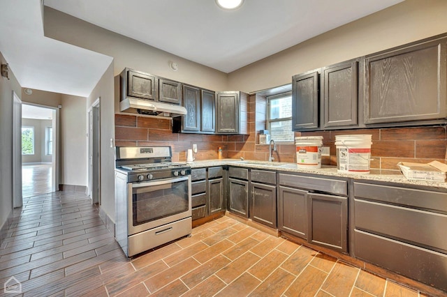 kitchen with backsplash, light stone counters, stainless steel range with gas cooktop, and sink