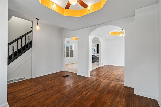 empty room with a tray ceiling, ceiling fan, and dark wood-type flooring