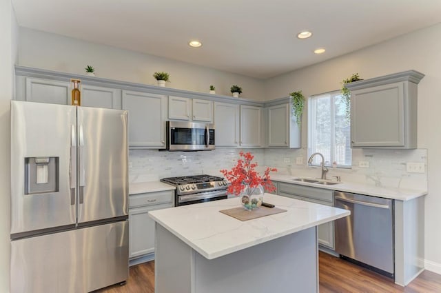 kitchen featuring appliances with stainless steel finishes, decorative backsplash, a center island, light stone countertops, and sink