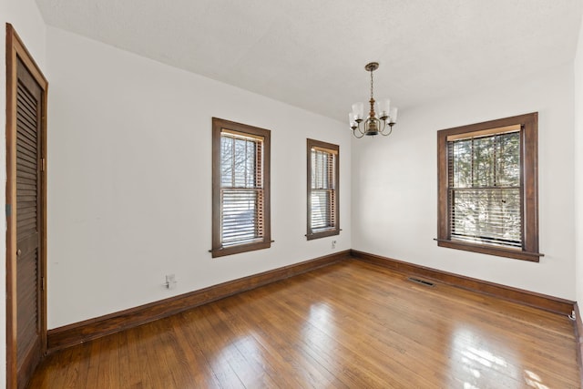 empty room with hardwood / wood-style floors and a chandelier