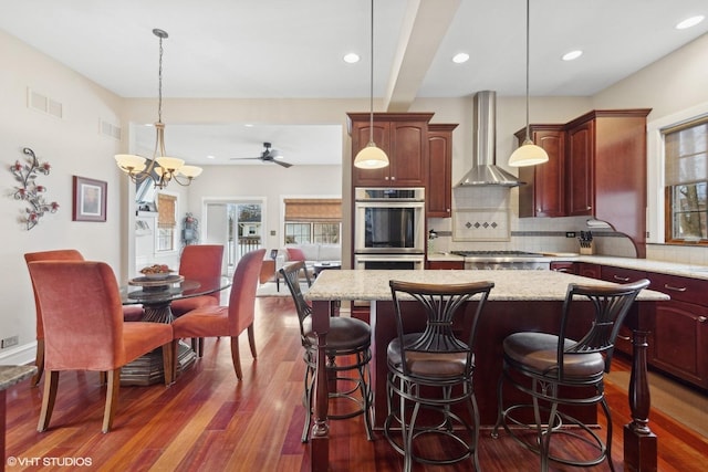 kitchen featuring wall chimney range hood, hanging light fixtures, stainless steel appliances, a center island, and tasteful backsplash