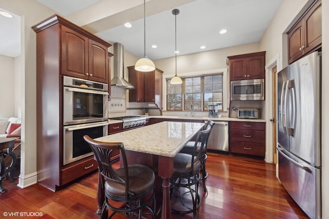 kitchen featuring backsplash, hanging light fixtures, stainless steel appliances, a center island, and wall chimney exhaust hood