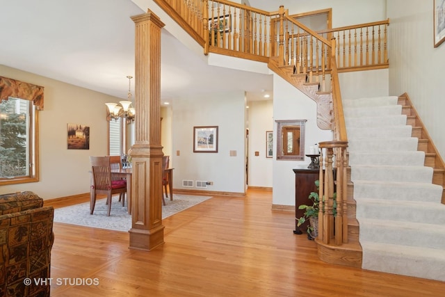 interior space with ornate columns, a towering ceiling, hardwood / wood-style flooring, and a notable chandelier