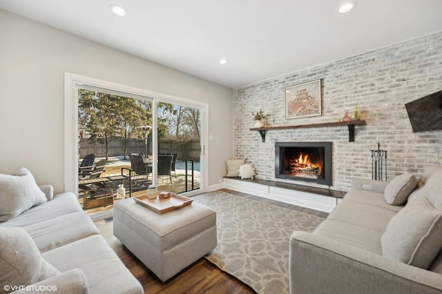 living room with a brick fireplace, wood-type flooring, and brick wall