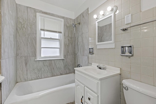 full bathroom with vanity, toilet, tile walls, and tiled shower / bath