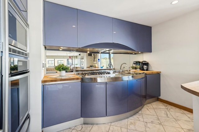 kitchen with stainless steel appliances, butcher block countertops, blue cabinetry, and plenty of natural light