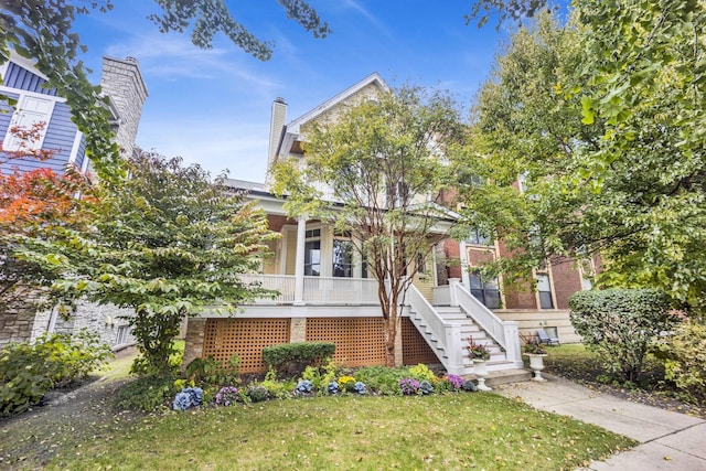 view of property hidden behind natural elements featuring covered porch and a front yard