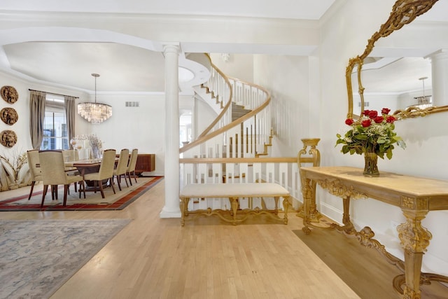 stairs featuring ornate columns, ornamental molding, wood-type flooring, and a notable chandelier