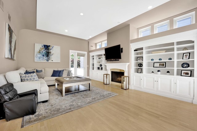 living room featuring built in shelves, light hardwood / wood-style floors, and a towering ceiling