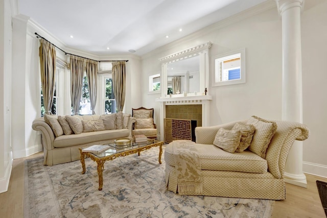 sitting room with light wood-type flooring, ornate columns, ornamental molding, and a tiled fireplace