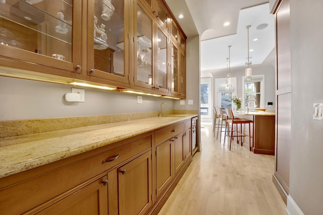 bar featuring decorative light fixtures, light stone countertops, sink, and light hardwood / wood-style flooring