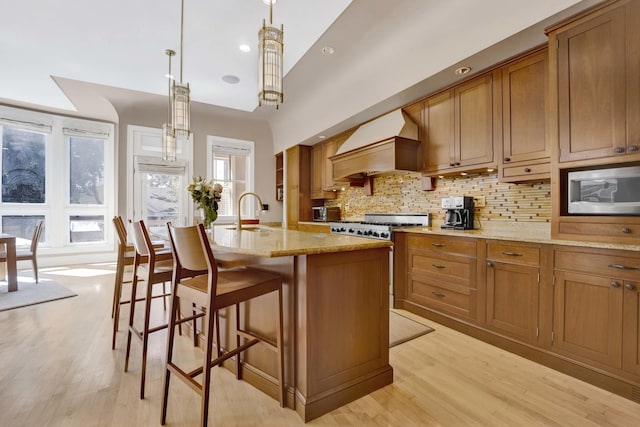 kitchen featuring custom exhaust hood, a kitchen island with sink, sink, high end stainless steel range oven, and decorative light fixtures