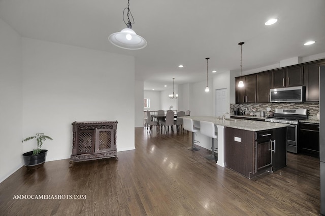 kitchen with dark brown cabinetry, sink, hanging light fixtures, an island with sink, and stainless steel appliances