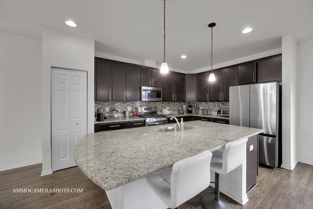 kitchen featuring dark brown cabinetry, sink, a center island with sink, pendant lighting, and stainless steel appliances