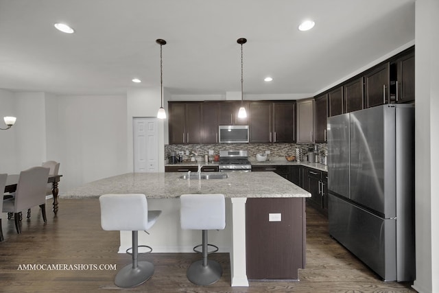 kitchen featuring pendant lighting, backsplash, dark brown cabinets, stainless steel appliances, and a center island with sink