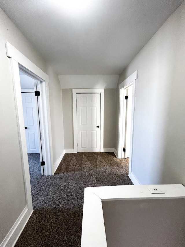 corridor featuring lofted ceiling and dark carpet