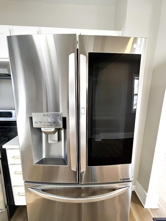 interior details with range, wood-type flooring, stainless steel fridge with ice dispenser, wall chimney exhaust hood, and white cabinets