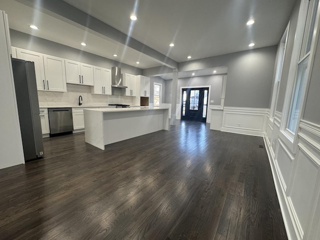 kitchen with white cabinets, wall chimney range hood, sink, appliances with stainless steel finishes, and dark hardwood / wood-style flooring