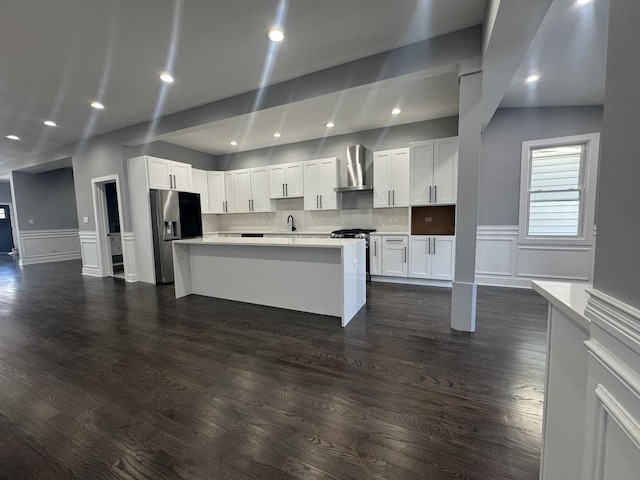 kitchen with stainless steel fridge, a kitchen island, white cabinetry, and wall chimney range hood