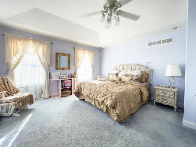 carpeted bedroom with a raised ceiling and ceiling fan