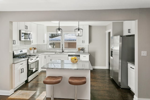 kitchen with stainless steel appliances, a kitchen island, white cabinetry, and pendant lighting