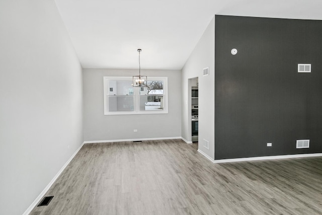 unfurnished dining area with vaulted ceiling, a chandelier, and hardwood / wood-style floors