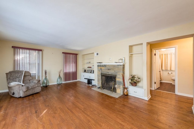 unfurnished living room with a stone fireplace, built in features, and hardwood / wood-style flooring