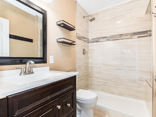 bathroom with toilet, tiled shower, and vanity