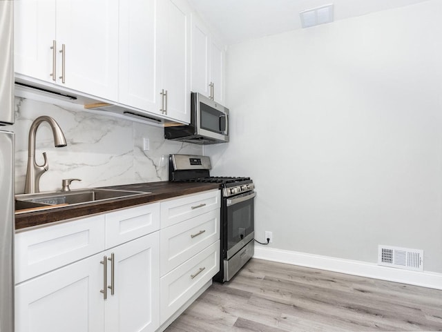 kitchen featuring stainless steel appliances, tasteful backsplash, white cabinets, light hardwood / wood-style flooring, and sink