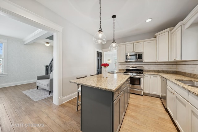 kitchen with white cabinetry, appliances with stainless steel finishes, light wood-type flooring, a kitchen island, and pendant lighting