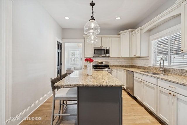 kitchen with stainless steel appliances, a center island, decorative light fixtures, light stone counters, and sink