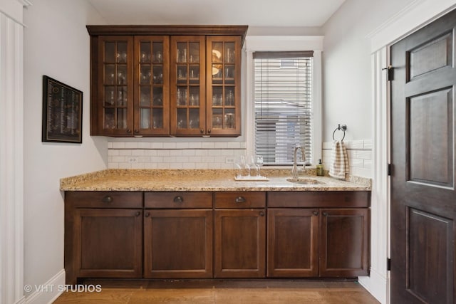 bar featuring decorative backsplash, dark brown cabinets, sink, and light stone counters