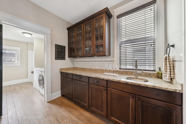 interior space featuring dark brown cabinetry, tasteful backsplash, sink, light stone counters, and light hardwood / wood-style flooring