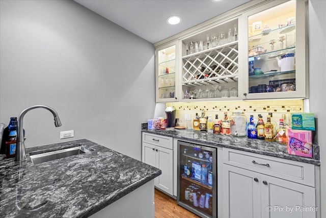 bar featuring decorative backsplash, beverage cooler, dark stone countertops, and sink