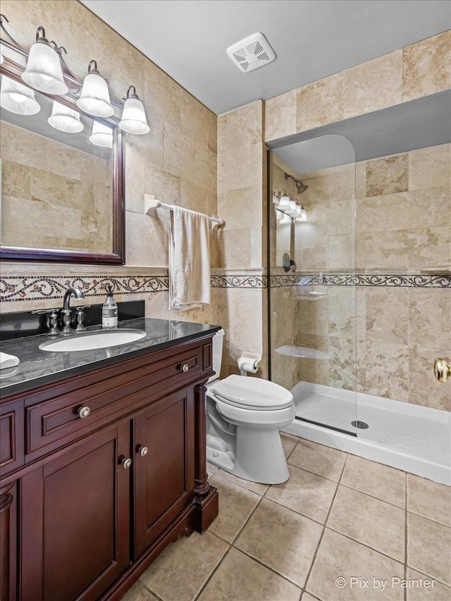 bathroom with vanity, tiled shower, tile walls, tile patterned flooring, and toilet