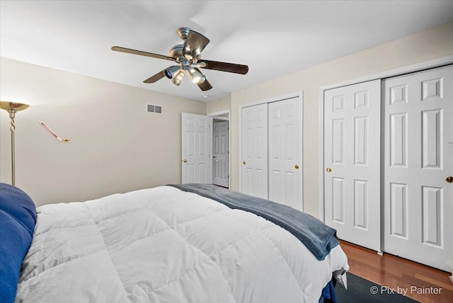 bedroom with multiple closets, ceiling fan, and dark wood-type flooring