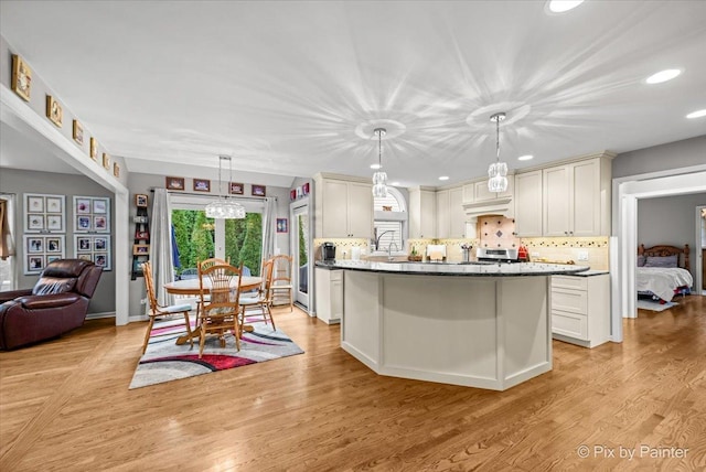 kitchen featuring pendant lighting, a center island with sink, stainless steel range, light hardwood / wood-style floors, and custom range hood