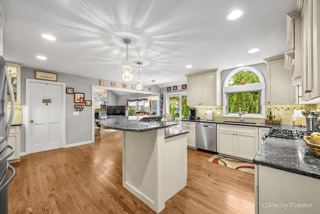 kitchen featuring sink, light hardwood / wood-style flooring, appliances with stainless steel finishes, tasteful backsplash, and decorative light fixtures