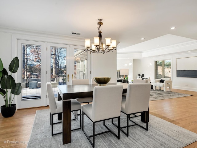 dining area with a tray ceiling, light hardwood / wood-style flooring, ornamental molding, and a chandelier