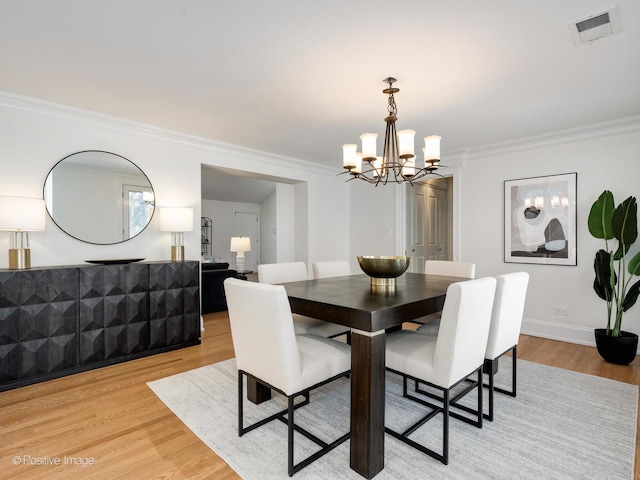 dining area featuring crown molding, light hardwood / wood-style floors, and a chandelier